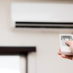 白いエアコンにリモコンを向ける女性
